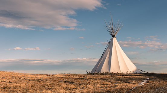 Traditional Native American nomadic teepee in the grassy plains at sunset and beautiful landscape background.
