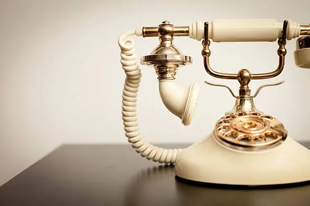 "Slightly desaturated color photo of a beautiful, antique, Victorian-style rotary telephone sitting on a table."