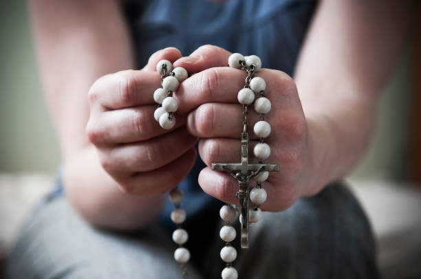 Hands of a young woman praying with rosary