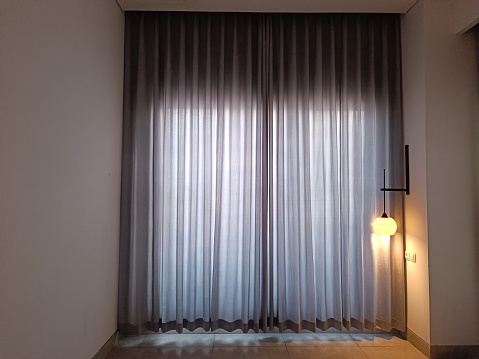 view of the curtains inside the hotel room with a little outside light coming in.  a dim lamp in the corner of the room hung on the wall