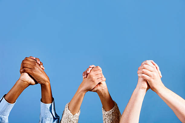 istock Three mixed pairs of clasped hands raised against sky blue 184397528