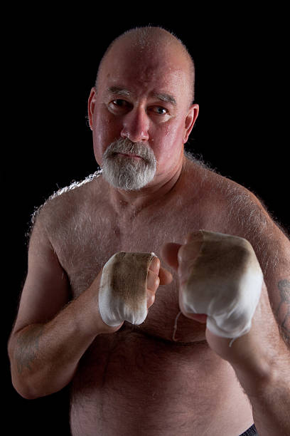 Old Champion Boxer Studio shot of an ex-boxer in his 60s reliving moments of glory. Focus on right fist. old man boxing stock pictures, royalty-free photos & images