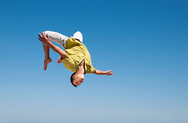 Man doing somersault in the air against blue sky Young man doing a somersault on the background of blue sky acrobatic activity stock pictures, royalty-free photos & images