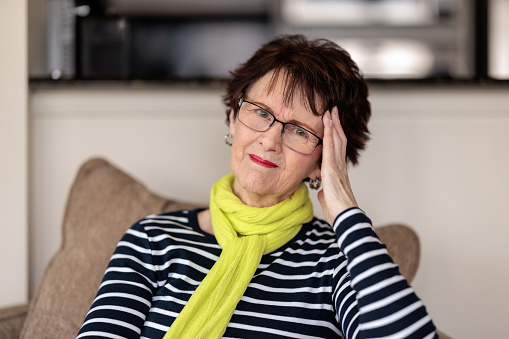 Senior woman sitting at home with hand on head and an uncomfortable expression.