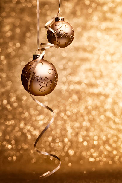 hanging golden Christmas baubles with curling ribbon on defocused golden glitter background