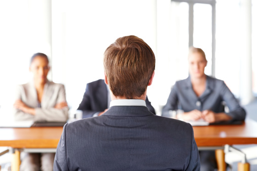 Businessman sits before three business people interviewing him. Horizontal shot.