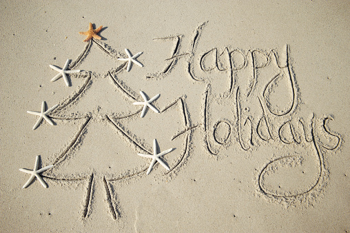 Happy Holidays message handwritten in smooth sand with simple holiday tree decorated with starfish