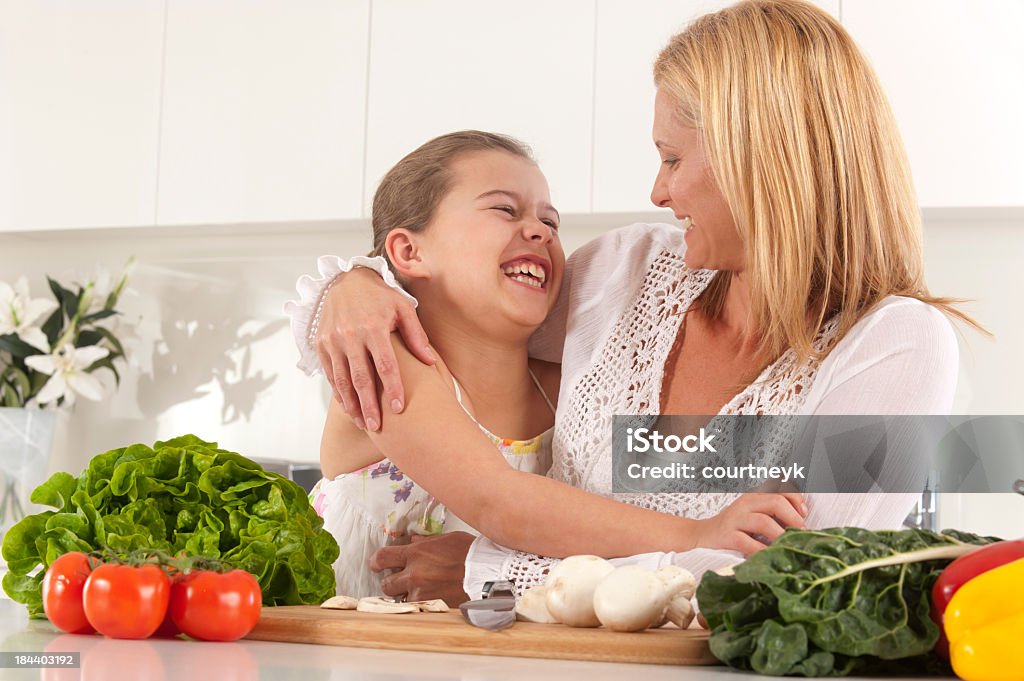 Young mother and daughter laughing preparing fresh vegetables Young mother and daughter laughing preparing fresh vegetables in the kitchen Adult Stock Photo