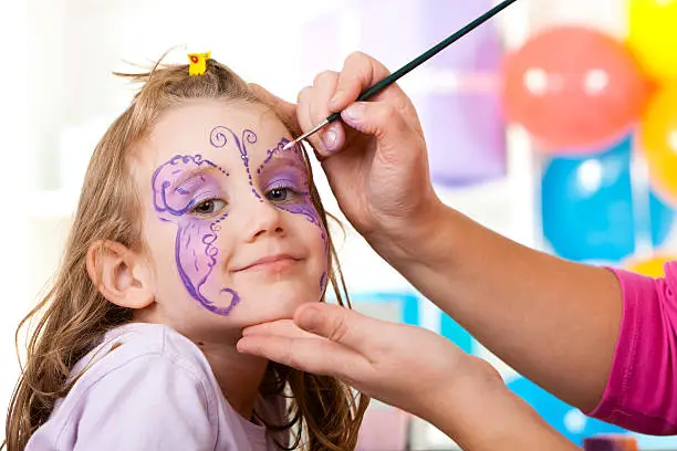 Little smiling girl having face painted on birthday party.