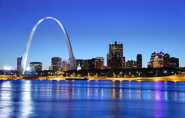 Night view of the arch in the St. Louis skyline The city of St. Louis, Missouri, as seen from across the river.  The Gateway Arch dominates the left upper section of the photo, more than twice as high as any of the buildings in the photo.  In a horizontal line across the background and behind the Gateway Arch are downtown buildings and some skyscrapers.  Lights are just coming on in the buildings even though there is still light in the sky.  A line of beach lies between the buildings and the river, which is a dark blue, mirroring the dark blue of the sky. mississippi river stock pictures, royalty-free photos & images