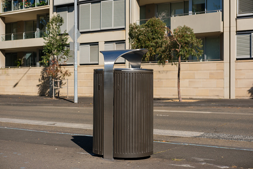 Brown metal rubbish bin outdoors beside a road.