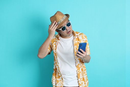Portrait of Asian energetic senior man holding a mobile phone isolated on the blue background with travel clothes. mature man, Asian man. Elderly, Holiday, Travel. studio shot. Multiple emotions.