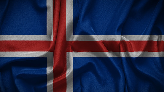 Icelandic flag in front of a mountain range partly covered by clouds