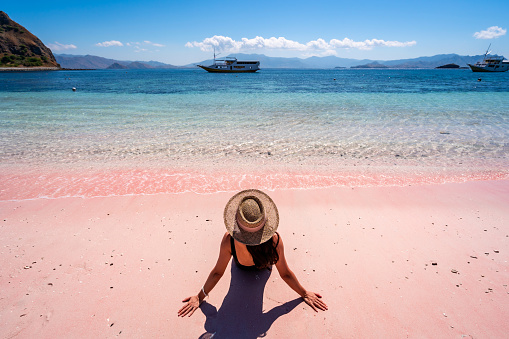 Young female tourism enjoying the tropical pink sandy beach with clear turquoise water at Komodo islands in Indonesia