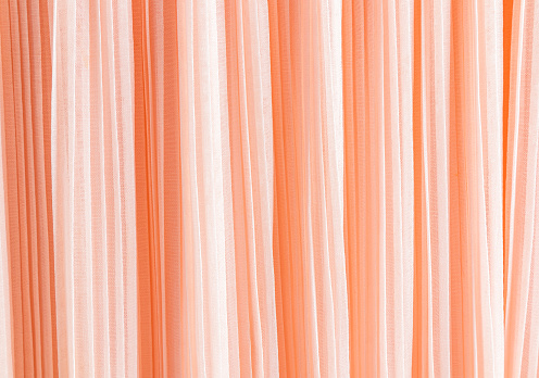 Delicate pleated pleats of silk fabric. Abstract background for design. Festive textiles. The trend of the color trend 2024 is peach fuzz