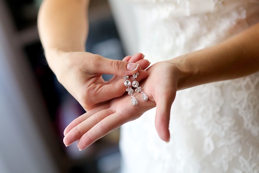 Women's hands of the bride in a wedding dress with earrings. Jewelry for the bride.