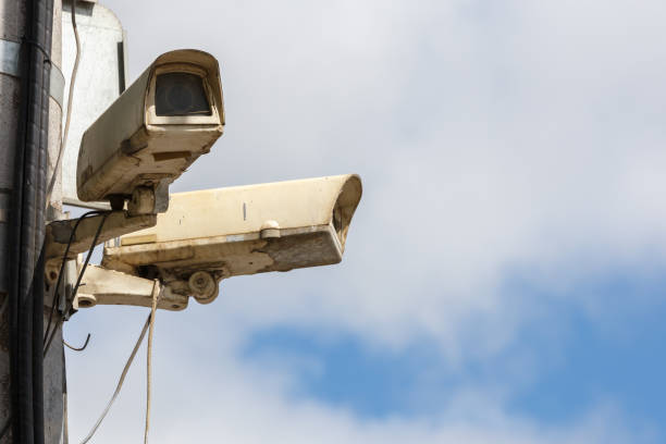 two old CCTV surveillance cameras on street pole at summer day