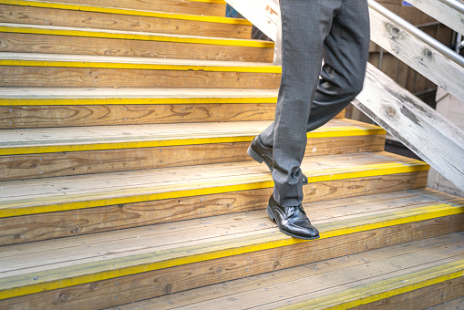A businessman in formal uniform suit and leather court shoe is walking down on the stair with hurry action. People in action photo, selective focus.