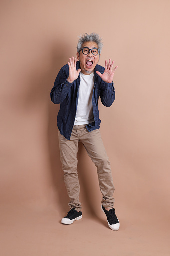 Portrait of Asian energetic senior man holding a mobile phone isolated on the blue background with travel clothes. mature man, Asian man. Elderly, Holiday, Travel. studio shot. Multiple emotions.