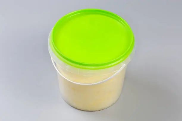 Banana-flavored cotton candy thicker consistency in the plastic container closed with green lid on a gray background