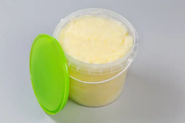 Banana-flavored cotton candy of thick consistency in the plastic container with removed green lid on a gray background