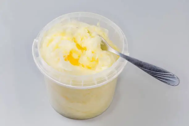 Banana-flavored cotton candy of thick consistency in open plastic container with dessert fork on a gray background