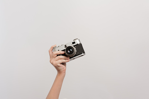 The raised hand of the photographer holds a retro camera