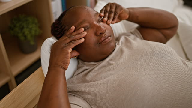 Tired african american woman, comfortably nestled in a relaxed bedroom setting, rubbing her eyes while lying on bed, waking up to the morning light.