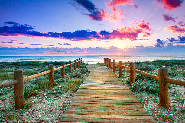Wooden walkway through grass to beach under colorful sky stock photo