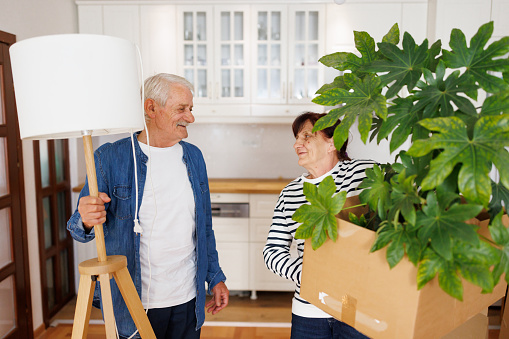 Front view of excited senior couple carrying belongings while moving into new apartment