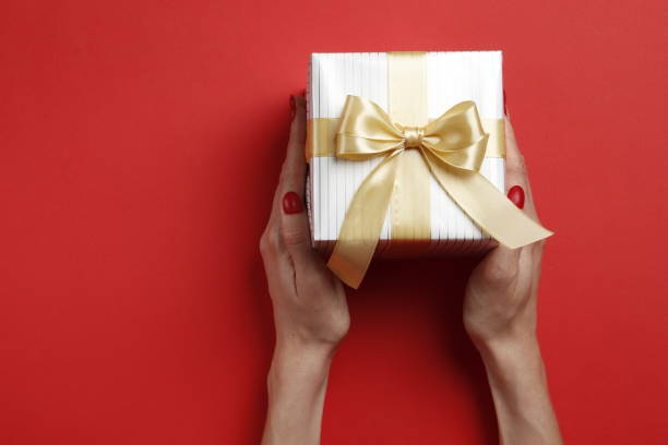 istock Festive gift box in a female hand on a red background. Place for text. 1844537754