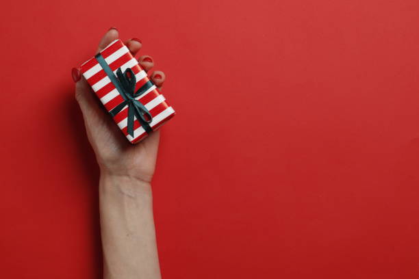 istock Christmas gift box in a female hand on a red background. Place for text. Top view. 1844537781