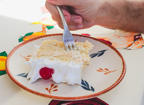 A man's hand holding a fork, eating a slice of cake. Birthday cake.