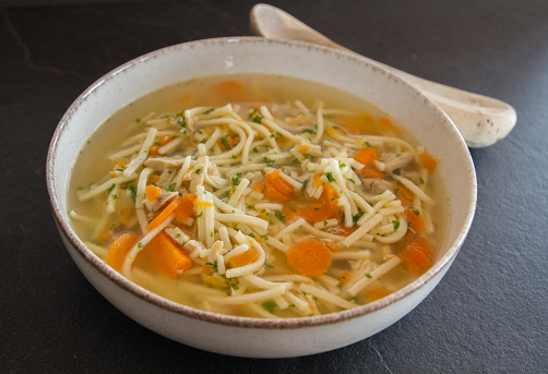 Simple traditional chicken noodle soup with carrots and parsley, ready to eat, european food, with wooden spoon