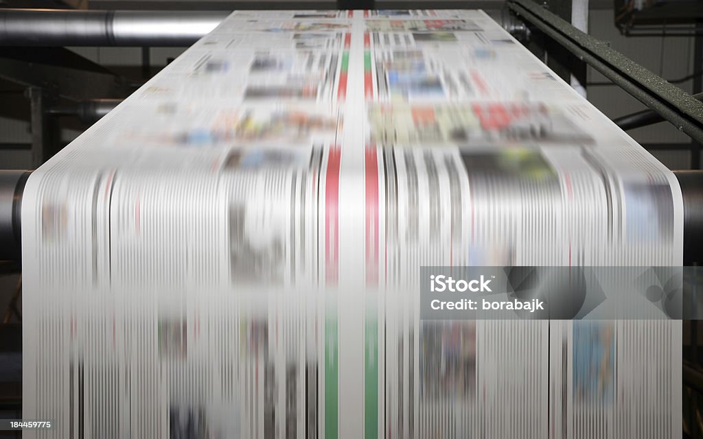 Offset printing press at work A large offset printing press running a long roll off paper over its rollers at high speed. Newspaper Stock Photo