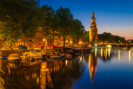 Montelbaan tower, Amsterdam, Netherlands. Evening cityscape. Dark sky and city lights. Dutch canals. Reflections on the surface of the water. Photography for design and wallpaper.