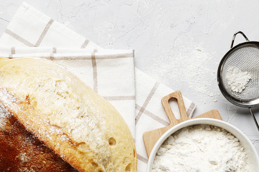 Homemade bread loaf, kitchen utensils and ingredients on a light table with place for text. Fresh bakery.