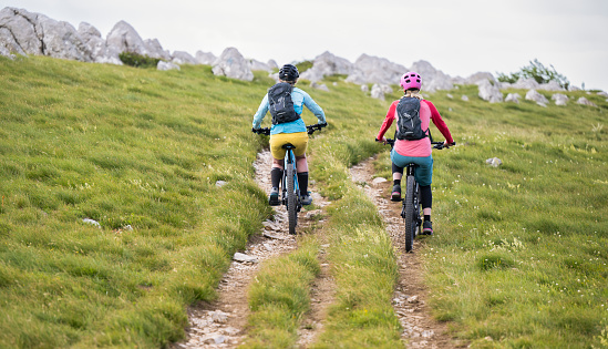 Two happy mid adult women wearing protective helmets riding electric mountain bikes together. Healthy lifestyle concept.