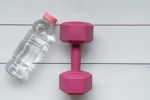 Fitness equipment.Dumbbells, bottle of water on white wooden background