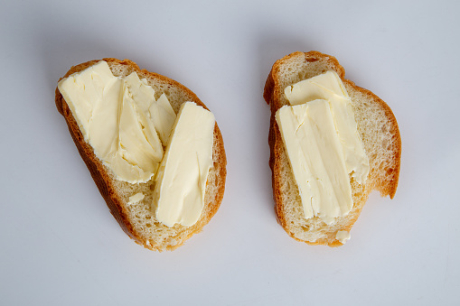 two pieces of white bread with butter on white background