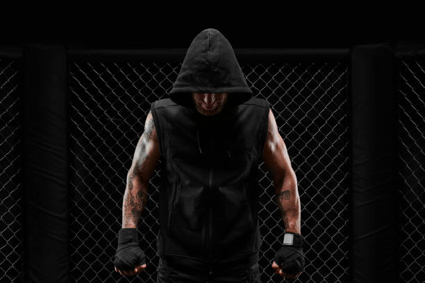 image conceptuelle d’un kickboxeur. un vrai combattant se tient dans la vraie cage de l’octogone. le concept d’idinemes mixtes, kickboxing, écoles de sport. - men sweat combative sport boxing photos et images de collection