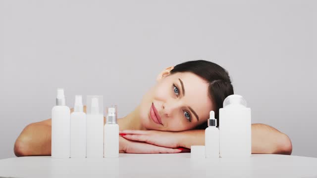 Cosmetics based on natural ingredients, scrub, tonic, body care. Production of natural cosmetics. A young woman on a light background among jars, bottles and tubes for cosmetic procedures.
