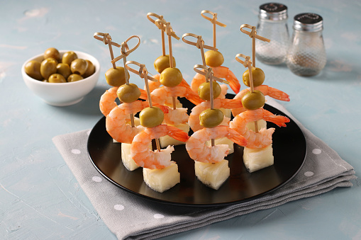 Canape with shrimp, pineapple and olives - festive bright appetizer on light blue background