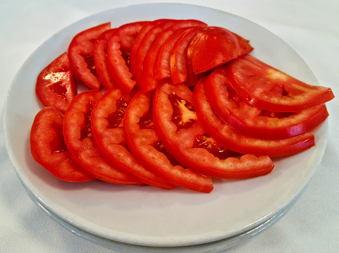 Many bright red cut tomato slices circle in plate