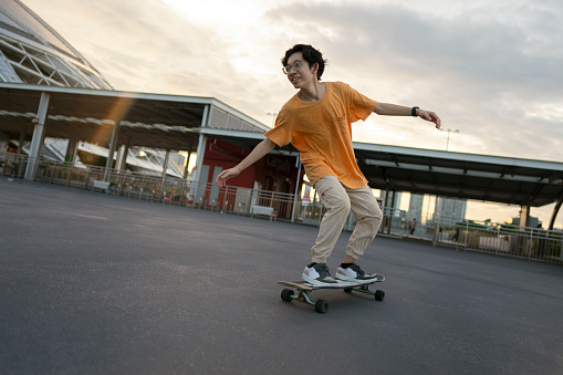 Young asian man longboard skating at sunset