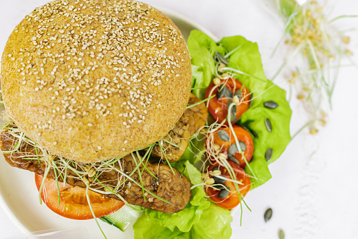 Homemade vegan tempeh burger with green salad, tomatoes and microgreens sprouts. Healthy  vegetarian food, suitable for weight loss and diet.