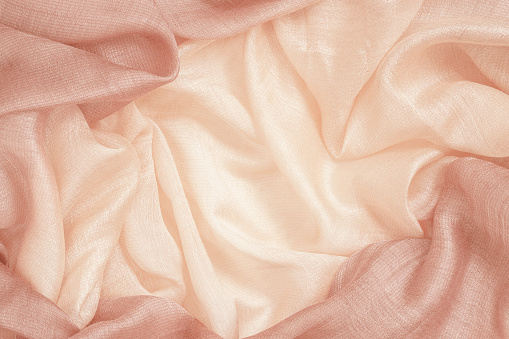 Crumpled silk fabric close up, peach color, soft texture, pastel textile background