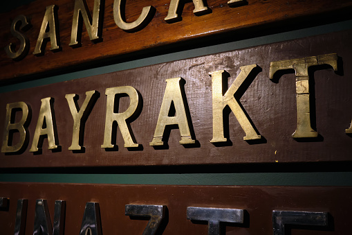 Close-up of large brass letters on wood panels. Names of warships of the Turkish fleet. Selective focus.