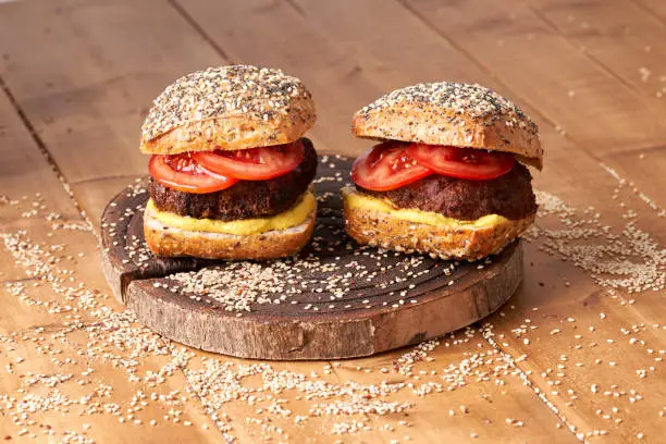 Homemade burger with tomatoes and mustard on the wooden table.