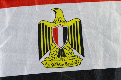 The national flag of Egypt, a tricolour consisting of the three equal horizontal red, white, and black bands, The flag bears Egypt's national emblem, the Egyptian eagle of Saladin in the white band, selective focus